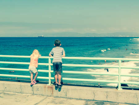 boy and girl watching ocean of Manhattan Beach, Los Angeles, CAの写真素材
