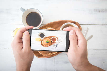photographing pancake with phone from topの写真素材