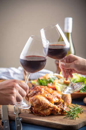 toasting with wine glasses in front of chicken dinnerの写真素材