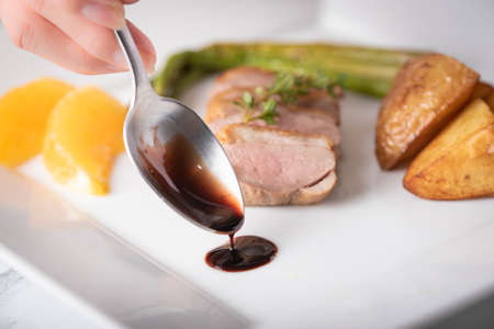 close up of chefâs hand decolating dish with red wine sauce の写真素材