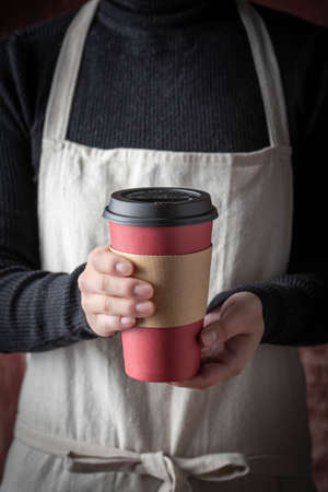 female with apron serving coffee with disposable paper cup