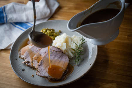 pouring gravy sauce on roasted pork with mashed potato and peasの写真素材