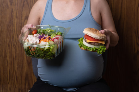 asian pregnant women holding healty salad and unhealthy hamburgerの写真素材