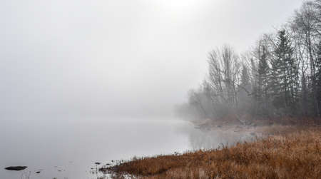 Heavy fog with diffused bright sunlight on Ottawa River.  Rapidly changing dense fog envelopes the bay - obscured sunshine beaming through fog, bright diffusion, mid-morning sunrise.の写真素材