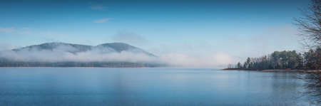 Fog rising from blue -   Panoramic view of dense fog lifting off the Ottawa River in the morning, blue sky, clear bright day with Laurentian hills in background.の写真素材