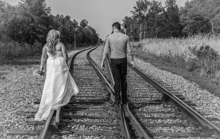 Newlywed couple walking on the rails of a pair of railroad tracks in black and white.の写真素材