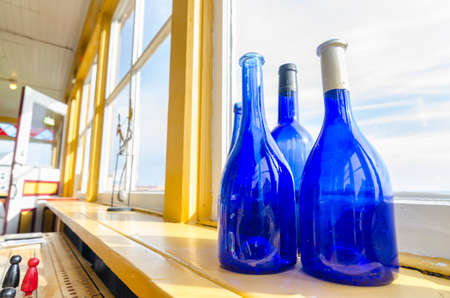 Blue bottles in a window beside the sea, Newfoundland Canada. Wide Angle view, Blue glass bottles decorate a shelf at a window with a view to the Atlantic in Grand Bank Newfoundland.の写真素材