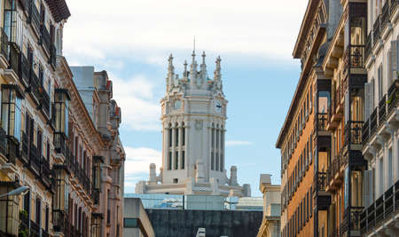 Clock on a watch tower of a church in Madrid, Spain.   Classic Spanish architecture flanked on each side by rows of warm colored apartment buildings.のeditorial素材