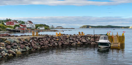 Golden adirondack chairs on a rock jetty.   Houses on the sea along a village shoreline.  Rural Newfoundland, Canada.  Docked speedboat waits in silence.の写真素材