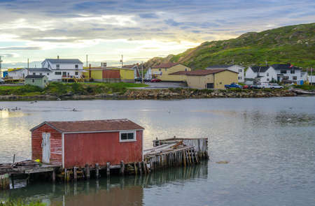 Little red shack on a dock in the small village and community of Twillingate, Newfoundland.  Sun sets brightly behind a hill in this coastal small Newfoundland community.の写真素材