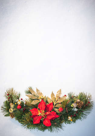 Christmas holiday faux poinsettia pine wreath adorned with gold leaf ribbon, Christmas balls and holly, resting on natural snow with white copy space.の写真素材