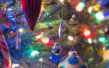 hristmas tree decorations.  Yellow, shiny finish, orb with blue circles, glows, surrounded by bright and vibrant multicolored mini-lights close up on a small faux indoor Christmas tree.の写真素材