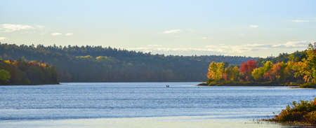 Two people floating in a small in the distance on the surface of a lake in summer late afternoon sun.  Late summer colors emboldened by late afternoon, golden sunlight.の写真素材