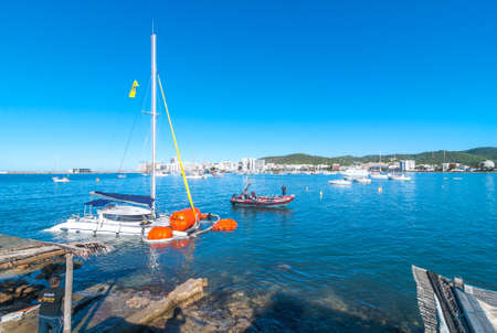 Editorial:  Sant Antoni De Portmany, Ibiza, November 6th, 2013:   Post thunderstorm blues.  Bright morning sees a dive crew work to recover a crippled, partially submerged catamaran boat after an overnight storm.のeditorial素材