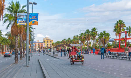 Barcelona, Spain, Nov 3rd, 2013: Tourism economy in Europe, people ride in a rickshaw, on bicycles & walking, taking advantage of warm weather.  Young people walk their dog along the city's palm tree lined roads.のeditorial素材