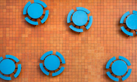 Orange square tile patio and empty, round blue tables in a random geometric shapes pattern