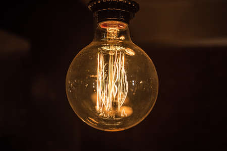 Large long electric incandescent filament in a retro style light bulb glows and reflects warm light.の写真素材