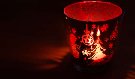 Christmas candle holder alight with a holdiay red glow, depicts scenes of winter and snow by the flame within.の写真素材