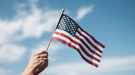Closeup of a woman's hand holding the American flag against blue skyの素材