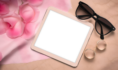 Tablet computer with glasses and pink rose petals on paper backgroundの素材