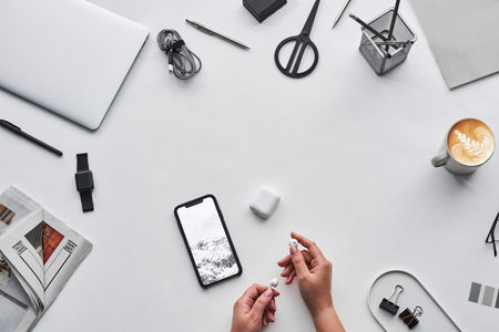 top view of woman using smartphone with blank screen and stationery on white table