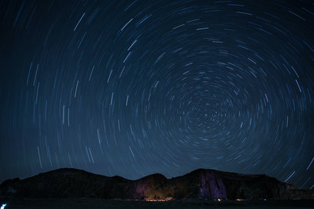 Star trails in the night sky with mountains and a lake in the backgroundの写真素材