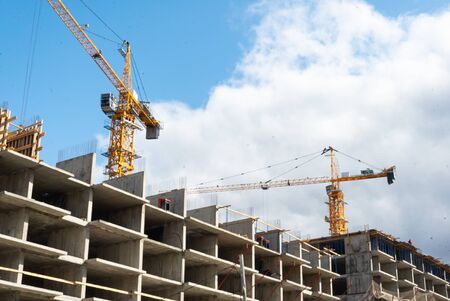 Tower building cranes and working builders on building multi-storey house.