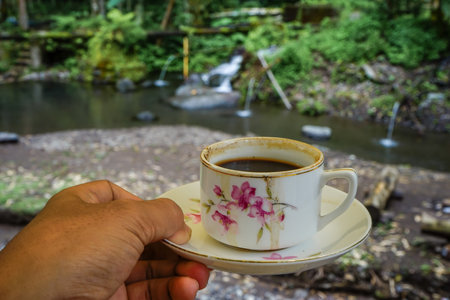 Hand holding a cup of coffee on the background of the waterfall.の写真素材