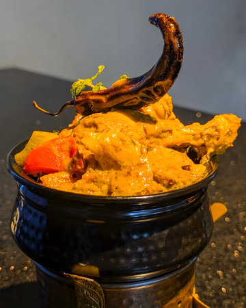 Rich and flavorful chicken curry served in a hammered copper bowl, topped with roasted chili and...