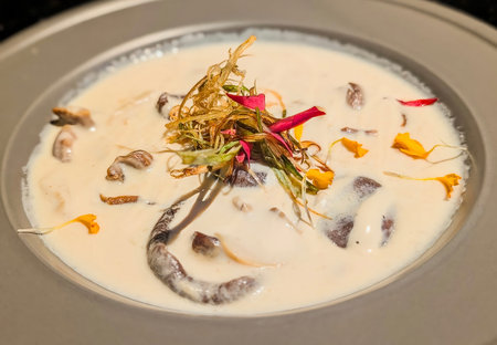 Close-up of a creamy Thai soup served in a black bowl, topped with colorful bell peppers, fresh herbs, and red chili garnish.の写真素材