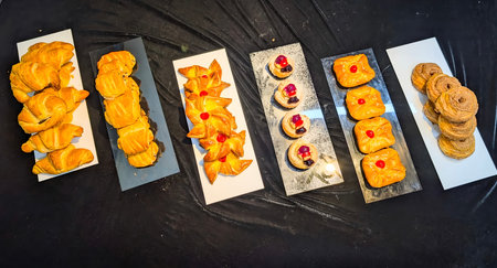 Top view of assorted freshly baked pastries displayed on elegant serving trays. The collection includes croissants, puff pastries, and fruit danishes with glossy golden crusts and vibrant toppings.の写真素材