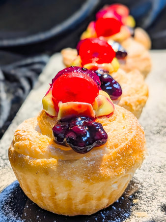 Close-up of freshly baked puff pastries topped with creamy custard, glazed cherries, and blueberry...