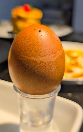 Close-up of a perfectly boiled brown egg placed upright in a glass egg cup. The image highlights the...