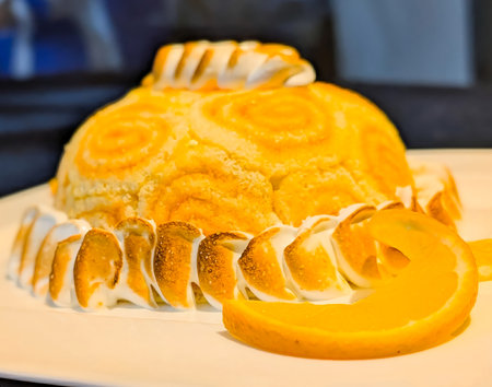 Close-up of an orange swirl rolled cake topped with toasted meringue and decorated with a fresh orange slice.の写真素材