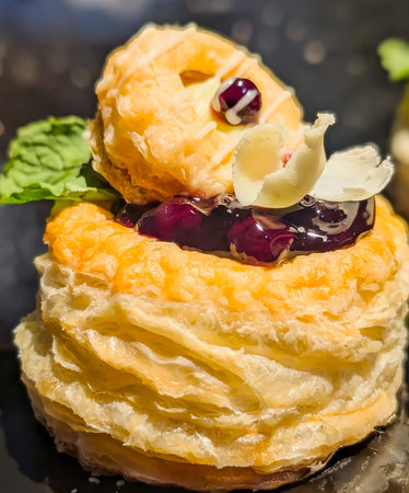 Close-up of a golden puff pastry filled with smooth cream and topped with glazed cherry and colorful candied fruits.の写真素材