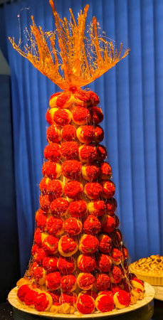 Elegant croquembouche dessert tower made of cream-filled choux pastry puffs coated with red glaze...