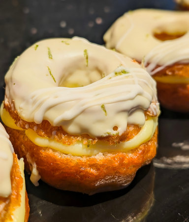 Row of freshly baked donuts topped with white almond glaze and pink swirl icing, filled with smooth cream and served on a white platter.の写真素材