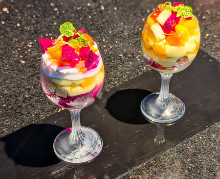 Vibrant tropical fruit parfait layered with dragon fruit, mango, kiwi, and whipped cream served elegantly in a tall glass.の写真素材