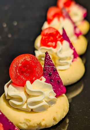 Elegant mini pastries topped with whipped cream, glazed cherries, and vibrant dragon fruit pieces,...