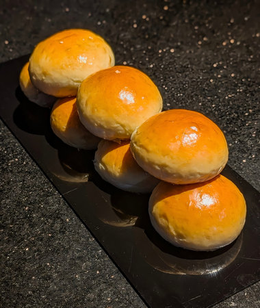 A visually striking stack of freshly baked, glossy brioche or milk buns, showcasing a rich golden-yellow color and smooth texture against a dark, dramatic background.の写真素材