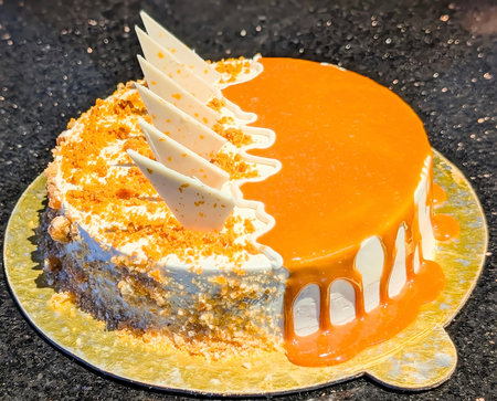 A luscious caramel drip cake decorated with white chocolate shards and crunchy biscuit crumbs, captured on a reflective board for a premium bakery look.の写真素材