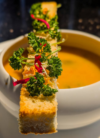 Delicate mushroom broth served in a modern white bowl, topped with herb-garnished focaccia and edible flowers.の写真素材