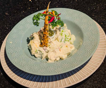 Visually striking creamy salad served in a light blue embossed bowl, featuring a cone-shaped sesame crisp, parsley sprig, and edible flowers.の写真素材