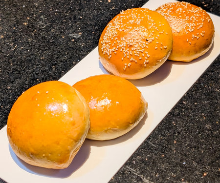 Freshly baked hamburger buns with a glossy golden surface, topped with white sesame seeds.の写真素材