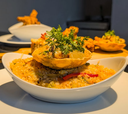 A vibrant bowl of vegetable fried rice topped with a crispy edible shell filled with creamy chicken curry, garnished with fresh herbs.の写真素材