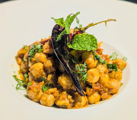 Seasoned chickpeas served in a modern white bowl, garnished with fresh cilantro and a whole dried...