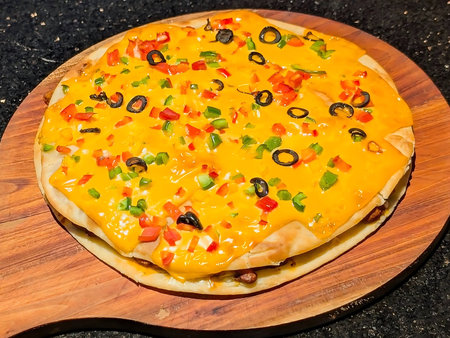 A vibrant Mexican-style layered pizza topped with melted cheddar cheese, black olives, bell peppers,...