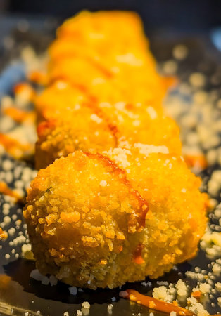 golden-brown fried cheese balls arranged in a line on a black rectangular plate, garnished with...