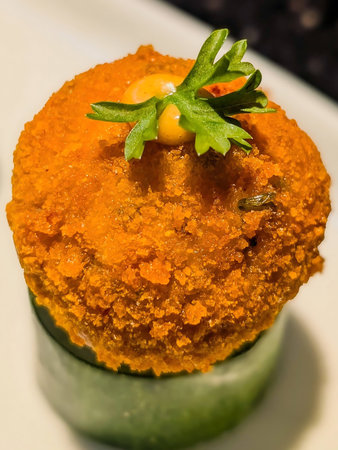 Golden-brown croquette placed on a fresh cucumber slice, topped with creamy sauce and parsley sprig.