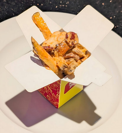 Indulgent serving of loaded fries topped with creamy orange sauce, sliced sausages, and mushrooms,...